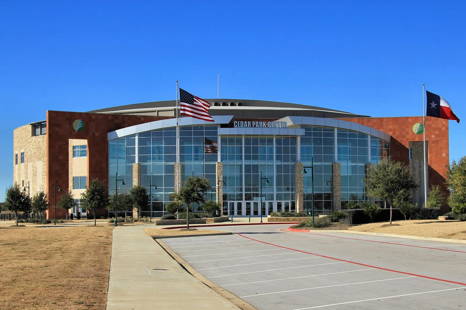 The Cedar Park Center arena with Texas and US flags under a clear blue sky in Cedar Park