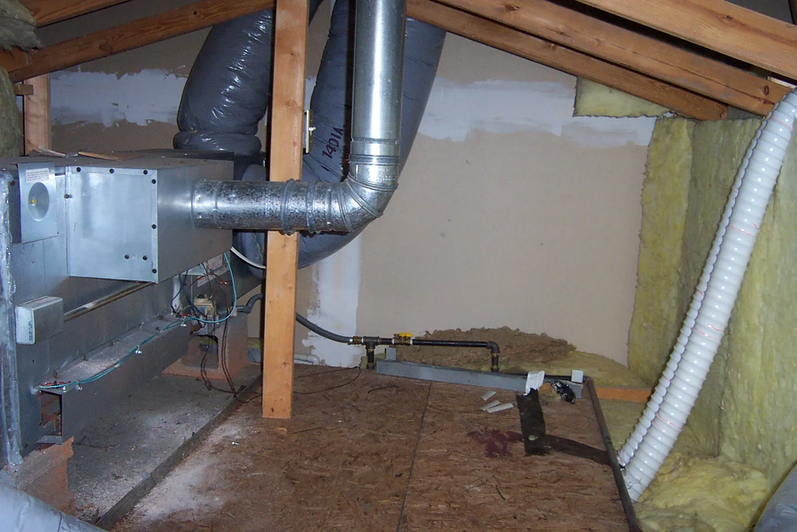 Horizontal gas furnace in a home attic with a metal flue pipe, gas line and flexible ducts