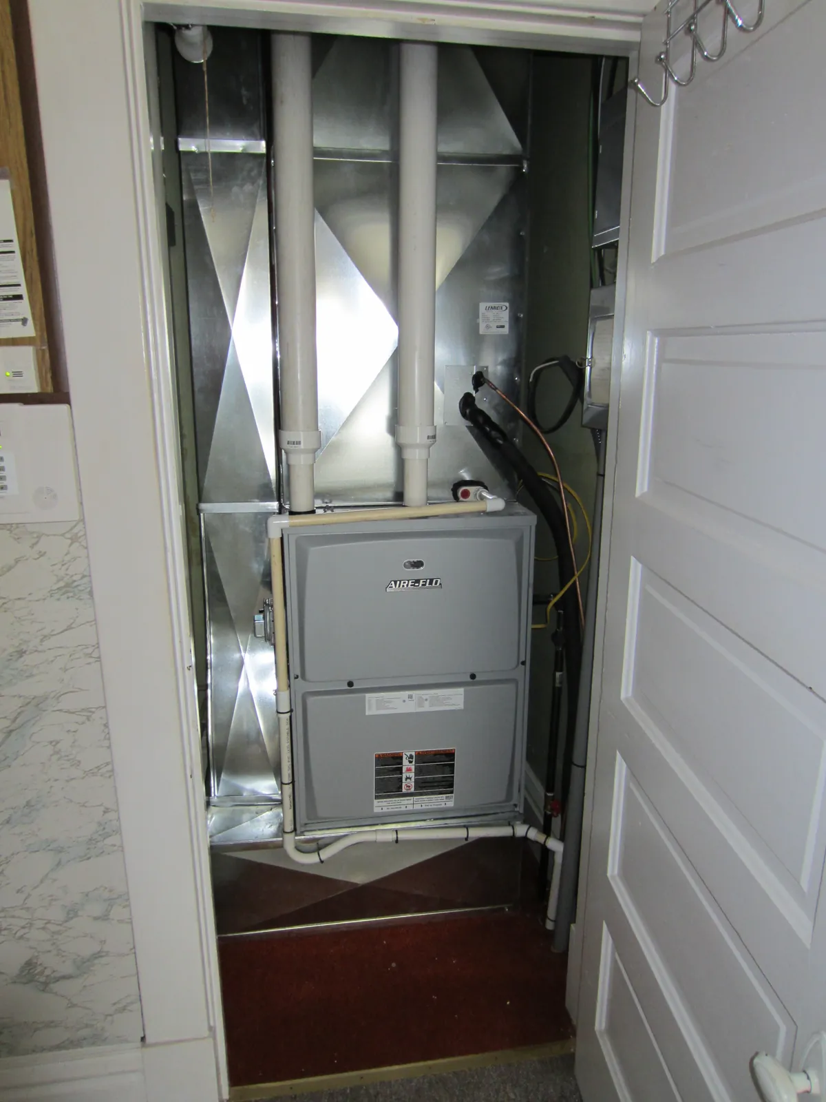 Upflow furnace and air handler installed in a hallway closet with PVC flue pipes and a sheet-metal supply plenum
