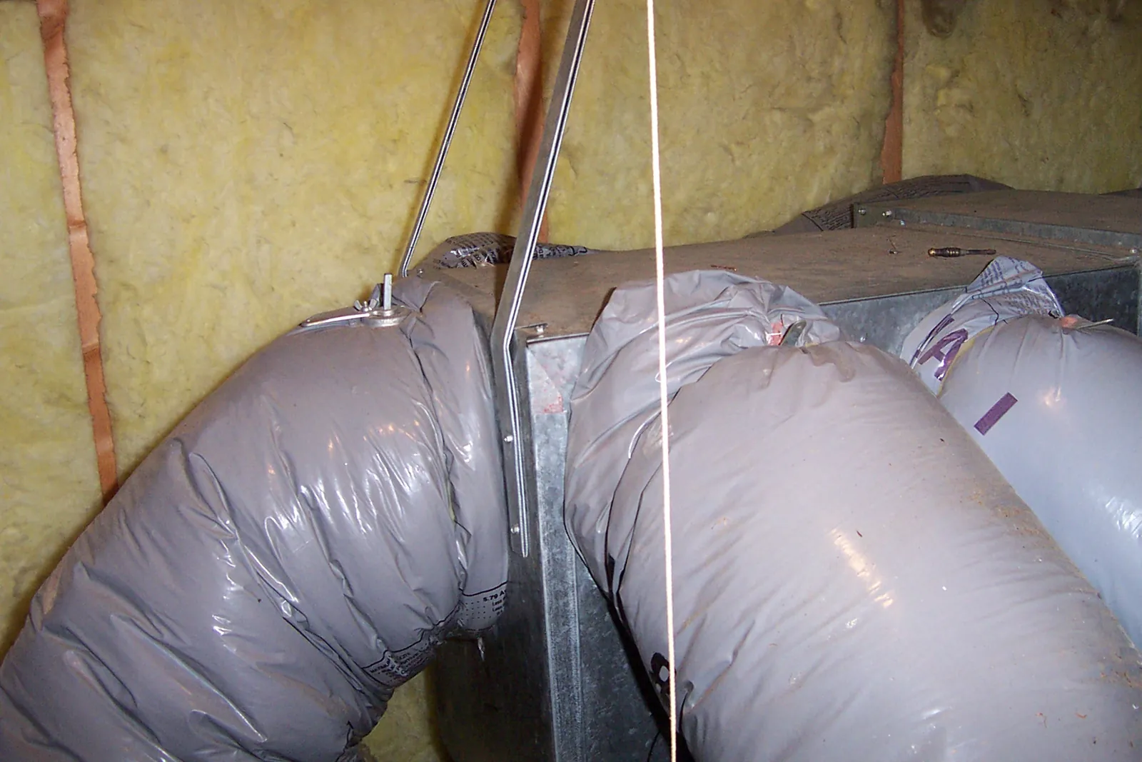 Insulated flexible ducts running off a supply plenum in an attic between fiberglass batts